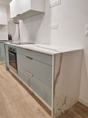 Marbled ceramic countertop, set on a blue-green kitchen cabinet with bronze handles. A miter cut and marbling veining follow-up were carried out.