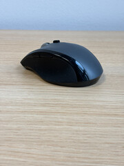 A black and gray computer mouse sits on a smooth wooden desk. The mouse is ergonomically designed...