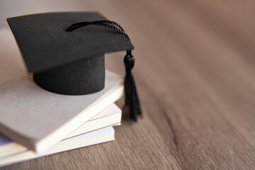 Graduation cap on top of stack of books on a wooden table. Copy space for text. Education concept.