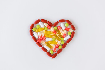 Group of pills in different colours arranged in a heart shape on a white background. Health care medical concept.