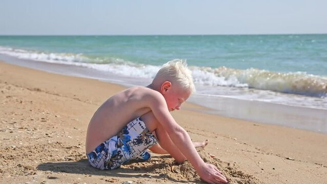 Cute white little boy play with sand on summer tropical beach. Vacation concept. Happy family and childhood