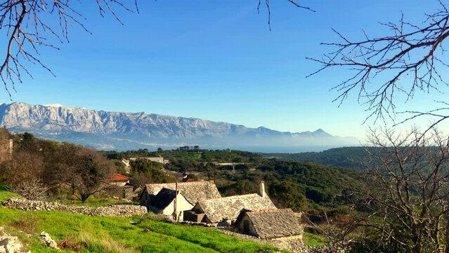 View of a little village with stone houses and a mountain range in the background. Dalmatia. Epic Panorama Nature. Dalmatian coast. Novo Selo, Brac Island, Croatia. Europe.