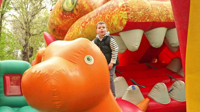 Child jumping on colorful playground trampoline. Kids jump in inflatable bounce castle on kindergarten birthday party Activity and play center for young child. Little boy playing outdoors in summer.