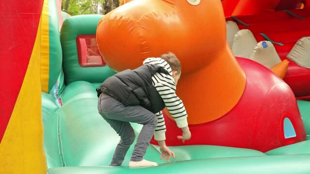 Child jumping on colorful playground trampoline. Kids jump in inflatable bounce castle on kindergarten birthday party Activity and play center for young child. Little boy playing outdoors in summer.
