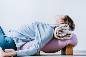 Woman doing restorative yoga with bolster, blanket and blocks
