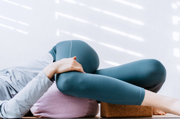 Woman doing yin yoga passive supine twists with bolster and cork block