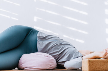 Woman doing yin yoga passive supine twists with bolster and cork block - obrazy, fototapety, plakaty