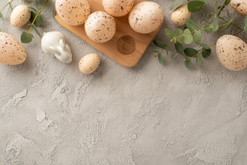 Top view sophisticated Easter theme featuring soft-hued eggs in timber crate, alongside porcelain bunny and lush eucalyptus sprigs, all set against a textured concrete grey surface with space for copy