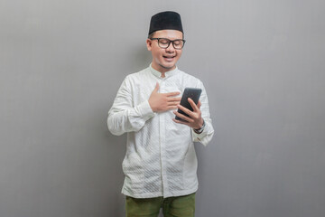 Portrait of an Asian Muslim man wearing a koko shirt and peci with shades of the fasting month,...
