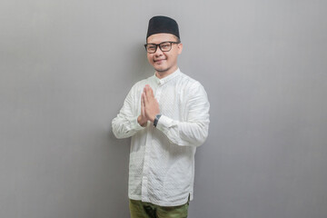 Asian Muslim man wearing a koko shirt and peci with shades of the fasting month, standing with Eid...