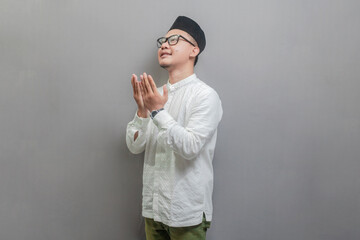 Asian Muslim man wearing a koko shirt and peci with shades of the fasting month, standing looking...