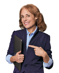 Mid-aged Caucasian with laptop in studio smiling and pointing aside, showing something at blank...