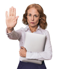 Mid-aged Caucasian with laptop in studio standing with outstretched hand showing stop sign,...