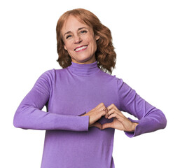Redhead mid-aged Caucasian woman in studio smiling and showing a heart shape with hands.