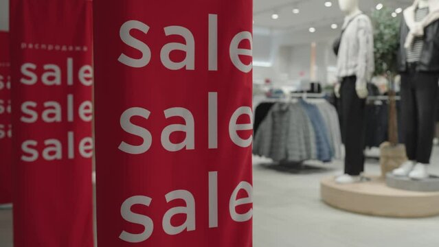 Sale sign at the entrance to clothing store - large red panels with white words. A row of SALE signs in a clothing store against the background of the sales floor, goods and mannequins.