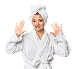 Caucasian woman in bathrobe and towel showing number ten with hands.