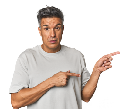 Middle-aged Latino man shocked pointing with index fingers to a copy space.