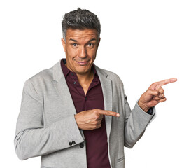 Middle-aged Latino man shocked pointing with index fingers to a copy space.