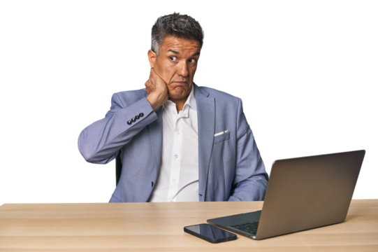 Elegant businessman at desk with laptop touching back of head, thinking and making a choice.