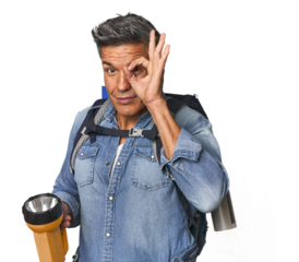Hispanic trekker with backpack and flashlight excited keeping ok gesture on eye.