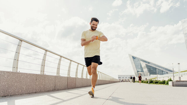 Man jogging in the city, checking time on his watch, focused on his fitness goals.