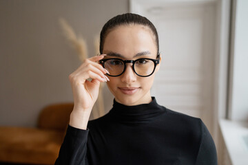 Confident young woman adjusting her stylish glasses, poised and professional.