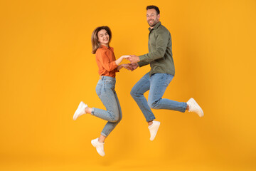 Fototapeta na wymiar Jubilant man and woman holding hands and jumping in excitement, capturing joyful moment in full-length shot against vibrant yellow background