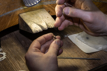 Close-up of a hand of a goldsmith who builds a precious jewel with valuable diamonds. To make the jewel it takes: precision, craftsmanship and patience. Concept of: gold, luxury.