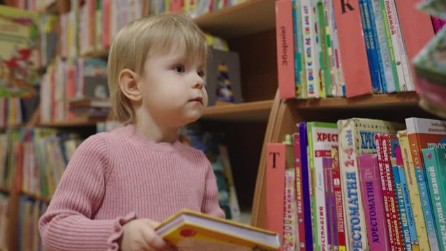 Charming little 2.5 year old girl for the first time in the children's public library. Concept of early child development.
