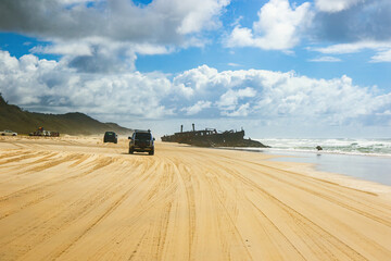 4WD trucks driving offroad on the Fraser island beach track near the SS Maheno shipwreck, half...