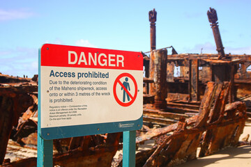 Danger sign prohibiting access to the SS Maheno shipwreck half buried in the sand of the 75 mile...