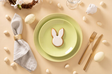 Easter table setting with white and green plate, bunny cookies, eggs on beige background. View from above. Happy Easter.
