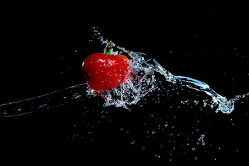 A red sweet pepper in splashes of water on a black background.