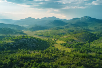 This aerial view captures a mountain range in the distance, showcasing the rugged peaks and valleys from above. The mountains are covered in shades of greens and browns, under a clear sky