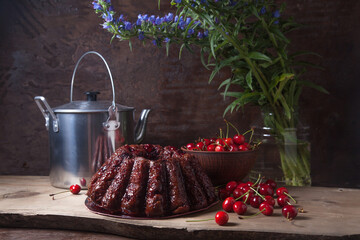 Delicious chocolate cake with sweet cherry, vintage kettle and bouquet of blue flowers on dark...
