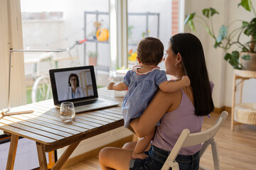 mother on her back with her daughter in her arms sitting on a video call with the doctor - virtual...