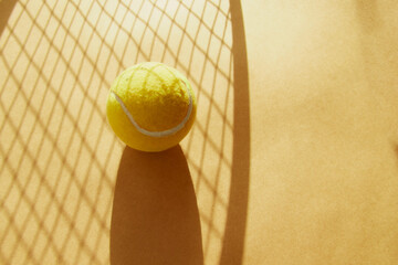 A yellow tennis ball lies in the shadow of a net for playing big tennis on a sandy background close-up