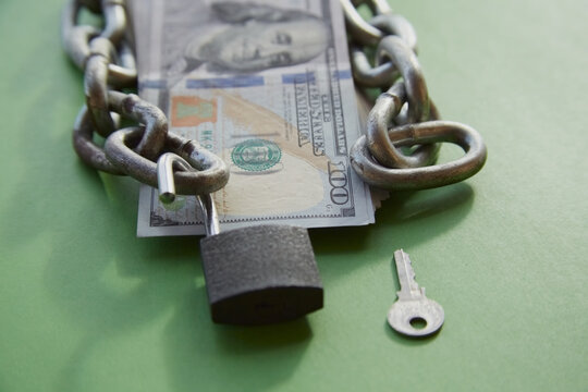  Hundred-dollar bills with a chain on them and an open lock and key nearby on green cloth, unlocking funds, unlocked money, unlocking an account
