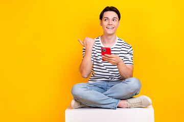Fototapeta na wymiar Photo of thoughtful dreamy man wear striped t-shirt writing sms modern gadget thumb empty space isolated yellow color background