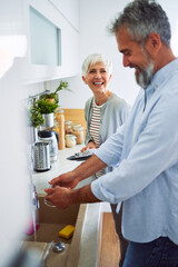 A joyful married senior couple having a laugh and washing the dishes together in the kitchen