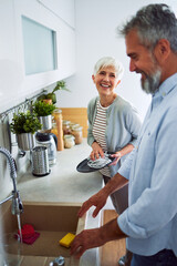 A happy senior adult wife helping her husband with the dishes while wiping a plate in the kitchen