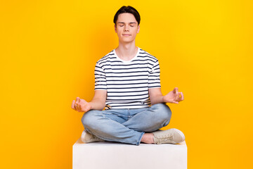 Fototapeta na wymiar Photo of dreamy funky man wear striped t-shirt closed eyes practicing yoga isolated yellow color background