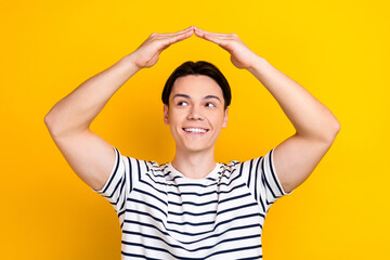 Portrait of nice student wear stylish t-shirt holding arms over head like roof look empty space isolated on yellow color background