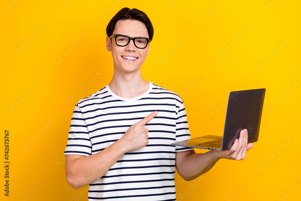 Canvas Prints Portrait of cheerful man with brunet hair wear stylish t-shirt in eyewear indicating at laptop isolated on yellow color background