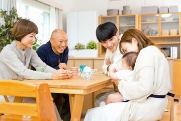 リビングの机を囲んで息子夫婦の赤ちゃんに喜ぶ祖父と祖母の家族