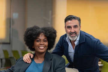 Cheerful man and woman colleagues posing with confidence and bright smiles in a modern office setting. 