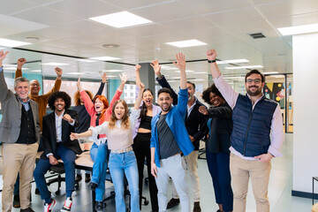 An enthusiastic team of office workers celebrating with raised arms in a vibrant coworking space. 