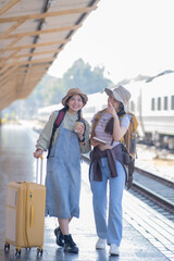 two young asian friends girls with backpacks at railway station waiting for train, Two beautiful women walking along platform at train station