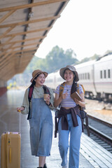 two young asian friends girls with backpacks at railway station waiting for train, Two beautiful women walking along platform at train station