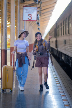 two young asian friends girls with backpacks at railway station waiting for train, Two beautiful women walking along platform at train station
